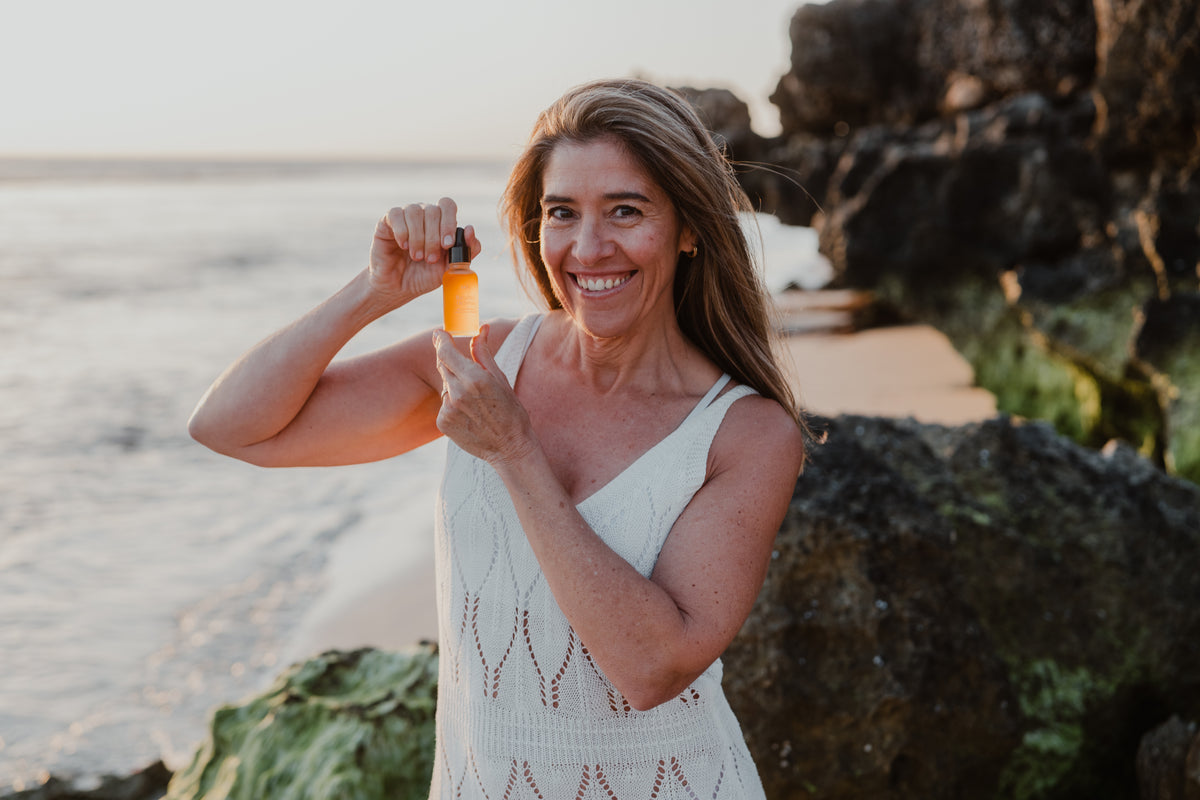 The cofounder of BTFY standing on a rocky beach at sunset holding up a BTFY Bakuchiol Oil Serum.